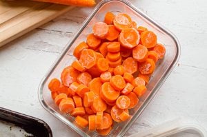 Frozen carrots in a rectangular glass container on a white tables.