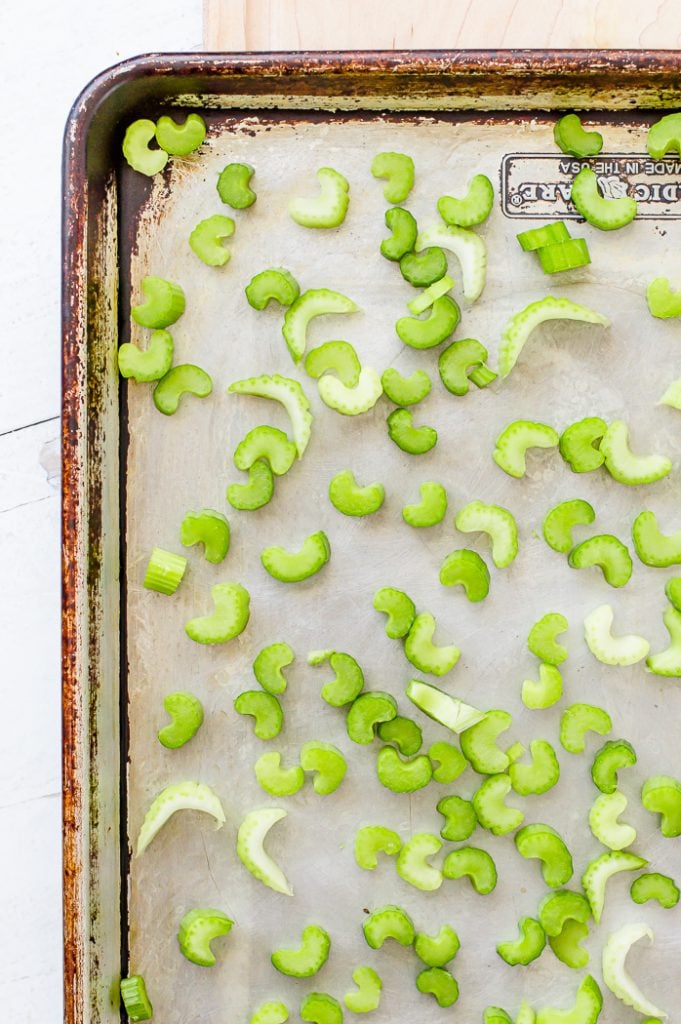 Sheet pan with chopped celery pieces spread out evenly in one layer. Sheet pan is sitting on a wooden cutting board on a counter.