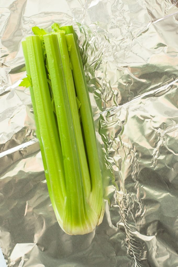 A whole bundle of celery is sitting on aluminum foil. Celery is in the center of the image. 