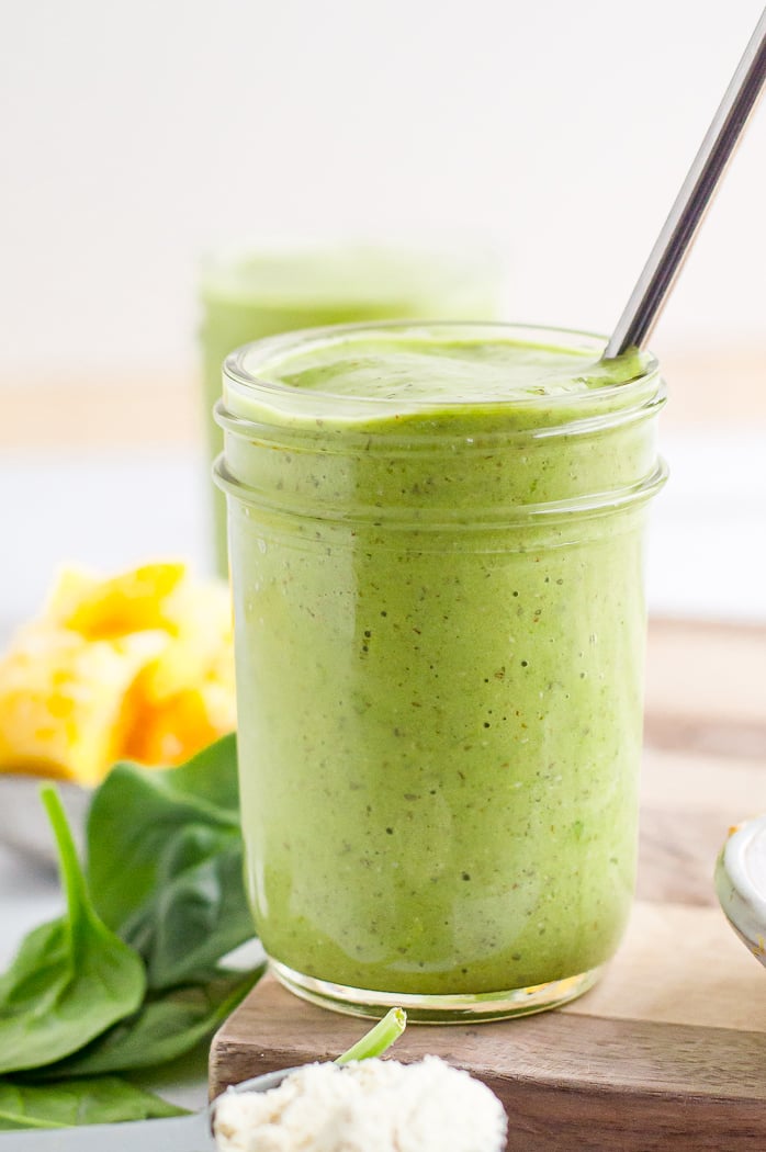 Green protein smoothie in a jelly jar with a metal straw.