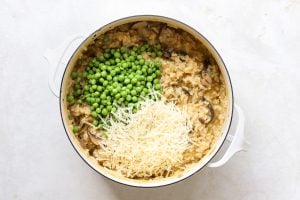 Mushroom risotto in a white pot with peas and grated parmesan cheese on top.