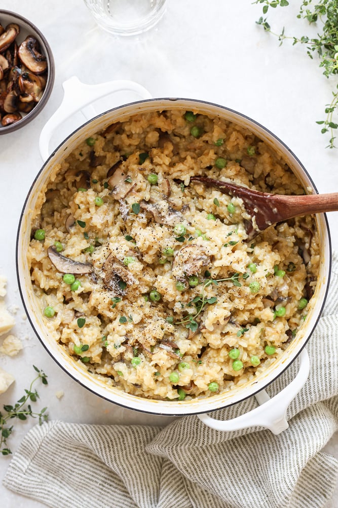 Cooked mushroom and pea risotto in a white pot with a wooden spoon and fresh thyme.