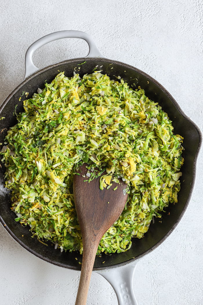 Le Creuset pan filled with finely chopped (shaved) Brussels sprouts. Wooden spoon in the shaved Brussels sprouts (as if stirring).