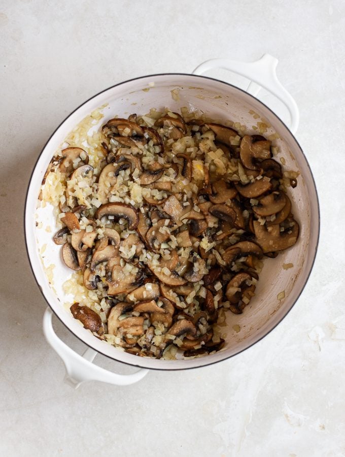 Sautéed mushrooms and onions in large white pot.