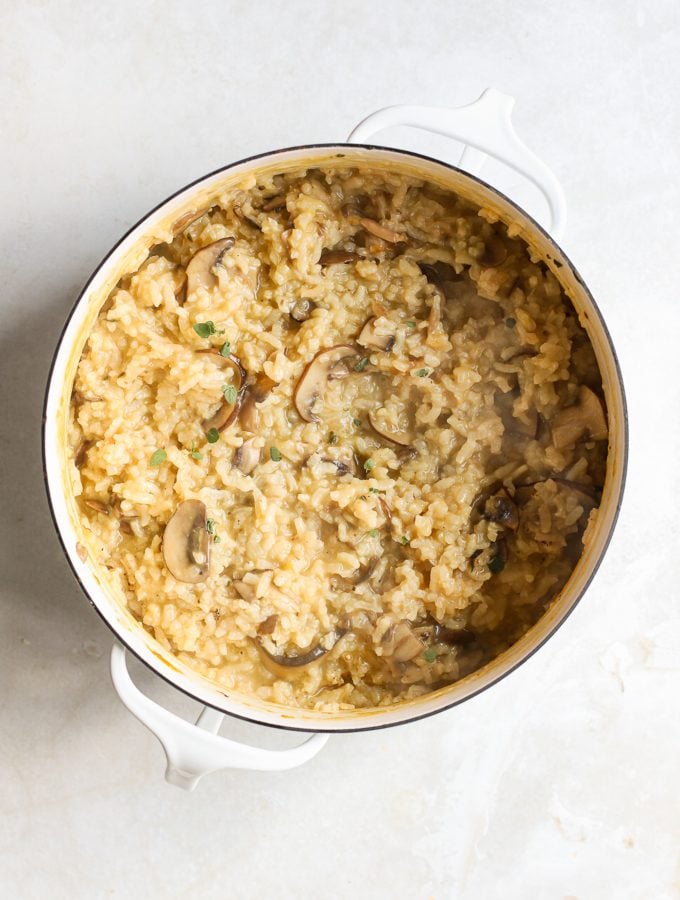 Cooked mushroom risotto  in a large white pot with thyme sprinkled on top.