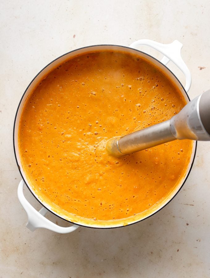 An immersion blender pureeing cooked carrot lentil soup after cooking.