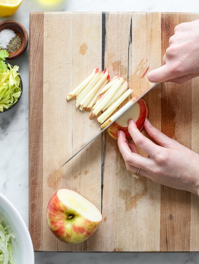 A person cutting an apple into matchsticks on a wooden cutting board with a knife. 