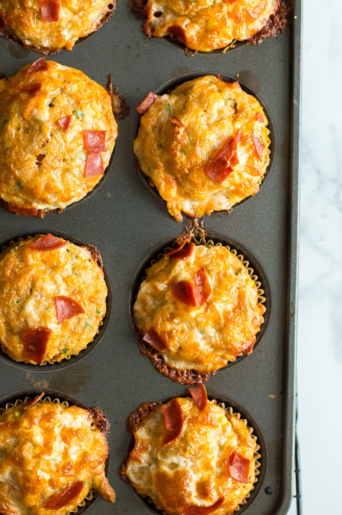 Baked pizza muffins fresh from the oven in a muffin tin on a white marble table. 