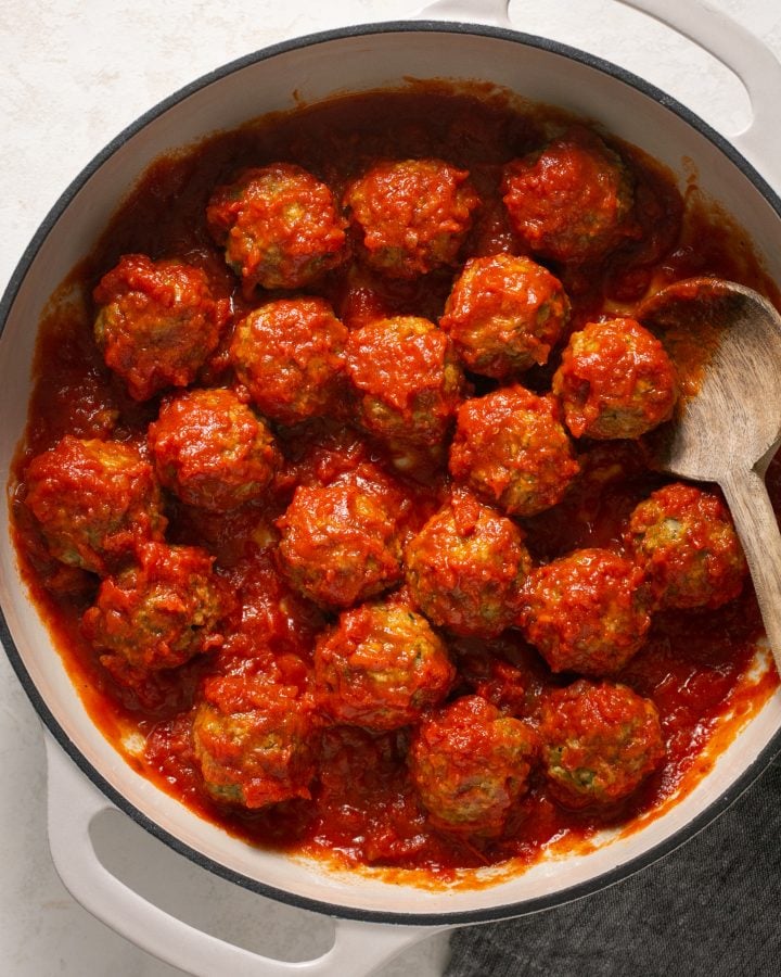 Eggplant meatballs with pasta sauce in a stockpot with a wooden spoon.