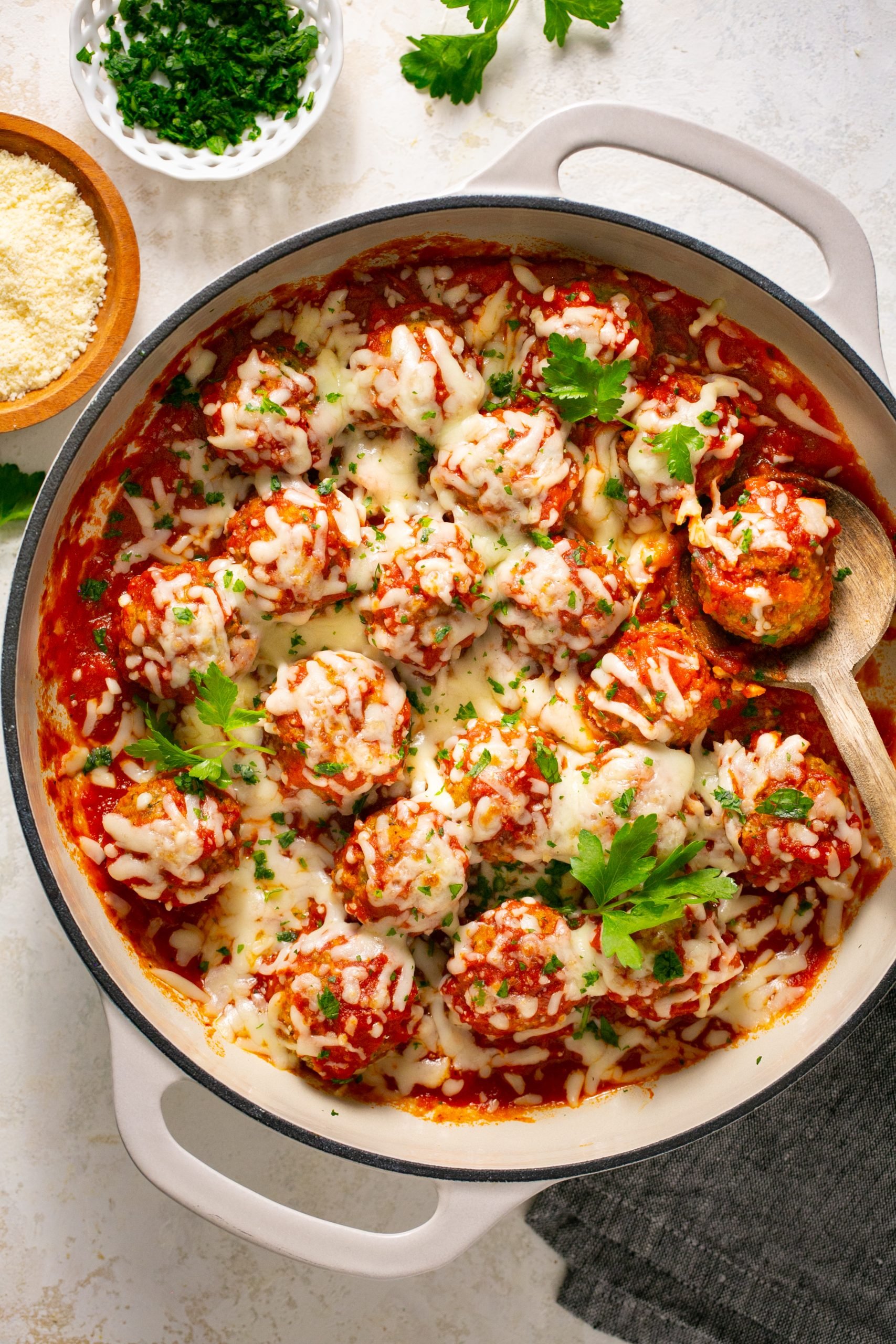 Eggplant meatballs in a white stock pot with a wooden spoon and topped with fresh parsley. 