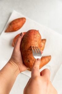 A person piercing a sweet potato with a fork.