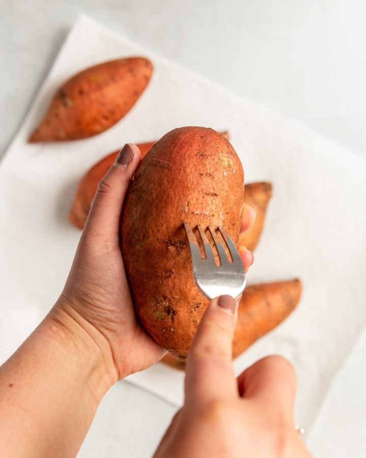 A person using a fork to puncture a sweet potato before baking. 