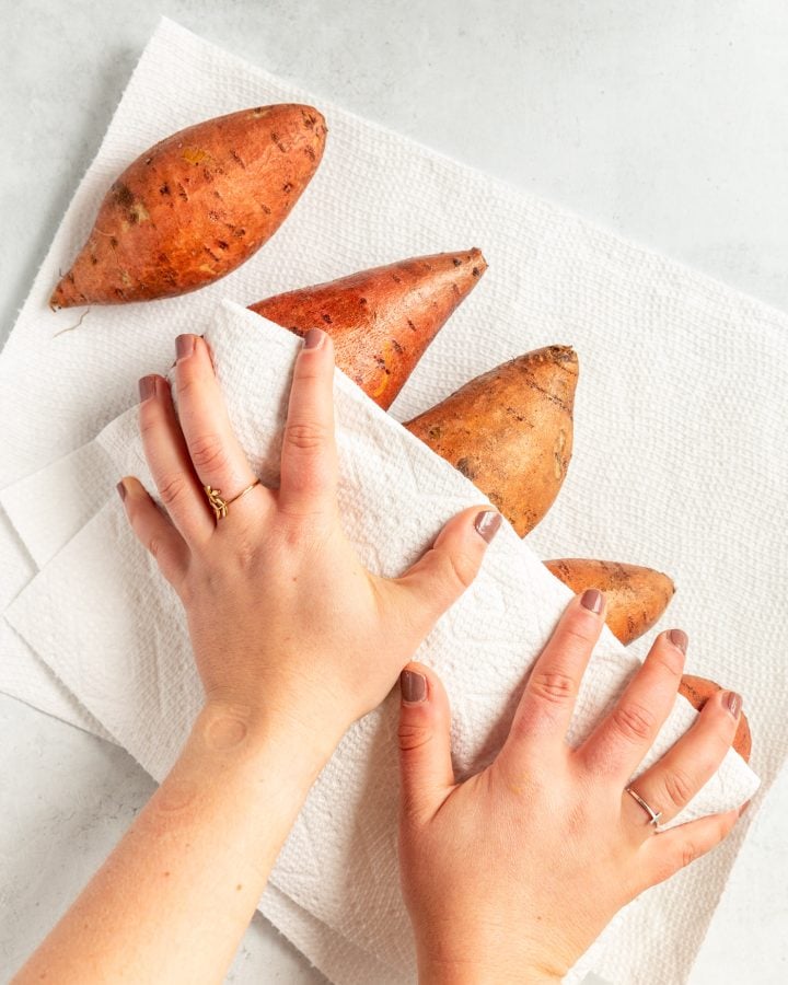 A person using paper towels to pat washed sweet potatoes dry.