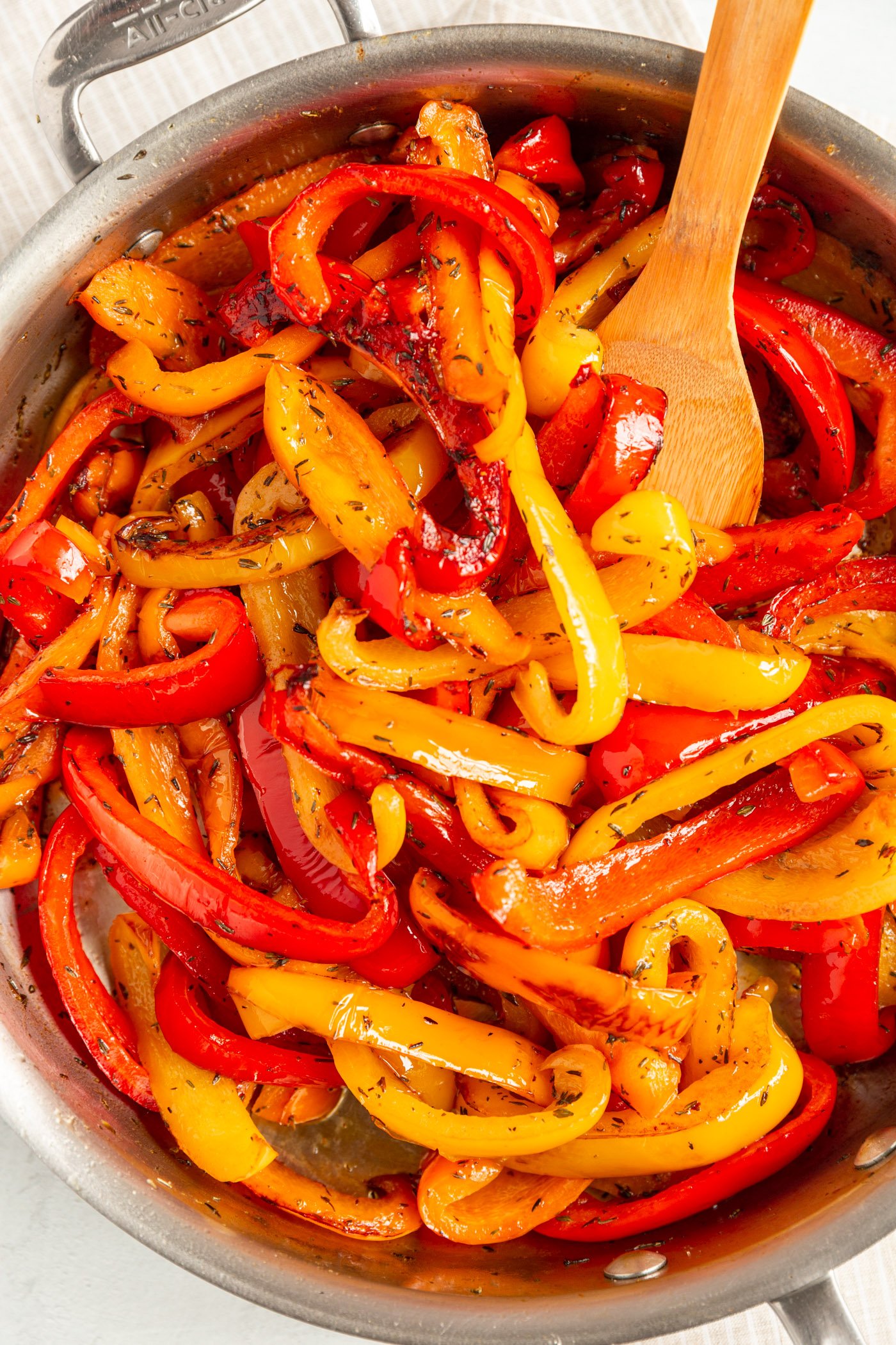 Sautéed bell peppers in a a skillet with a wooden spoon. 