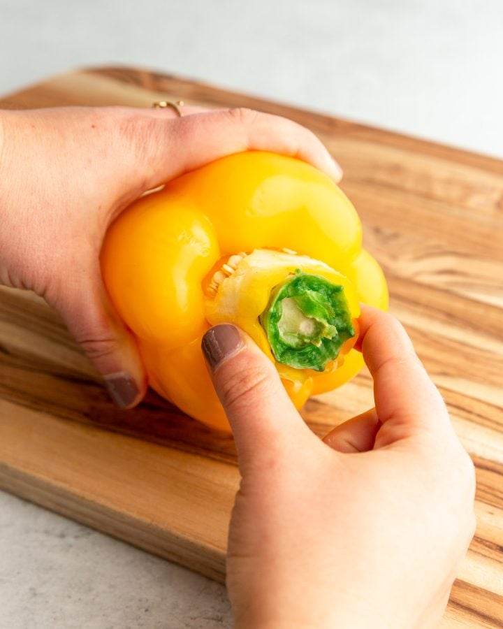 A person removing the core of a bell pepper on a wooden cutting board. 