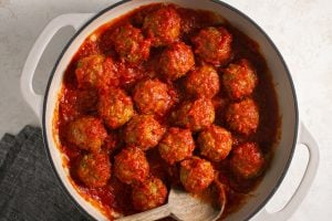 Eggplant meatballs with pasta sauce in a stockpot with a wooden spoon.