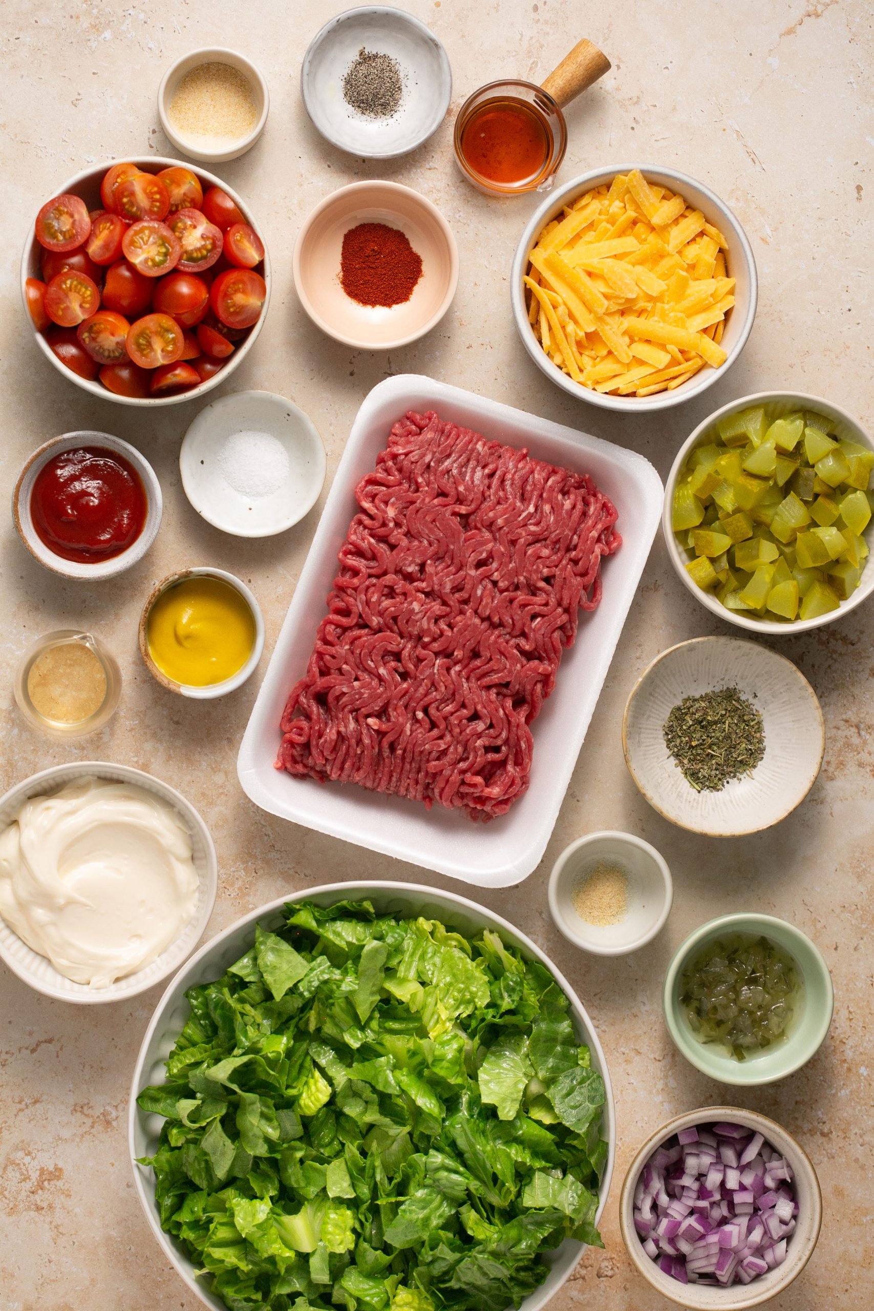 Ingredients for cheeseburger salad in small bowls on a table before being made into the salad. 