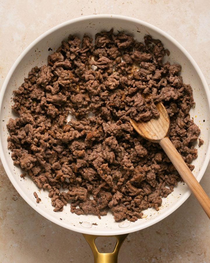 Cooked ground beef in a skillet with a wooden spoon