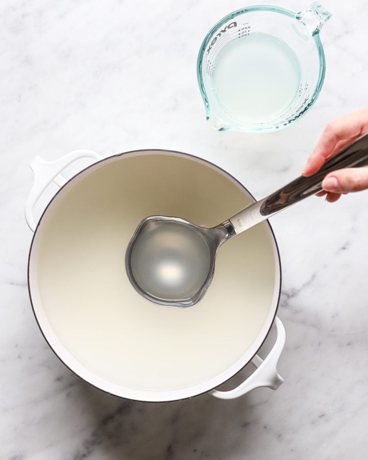 A person using a ladle to reserver pasta water