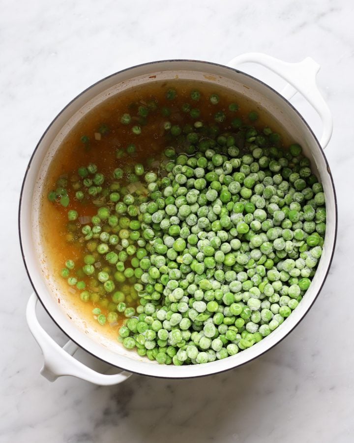 Broth and frozen peas in a white dutch oven.