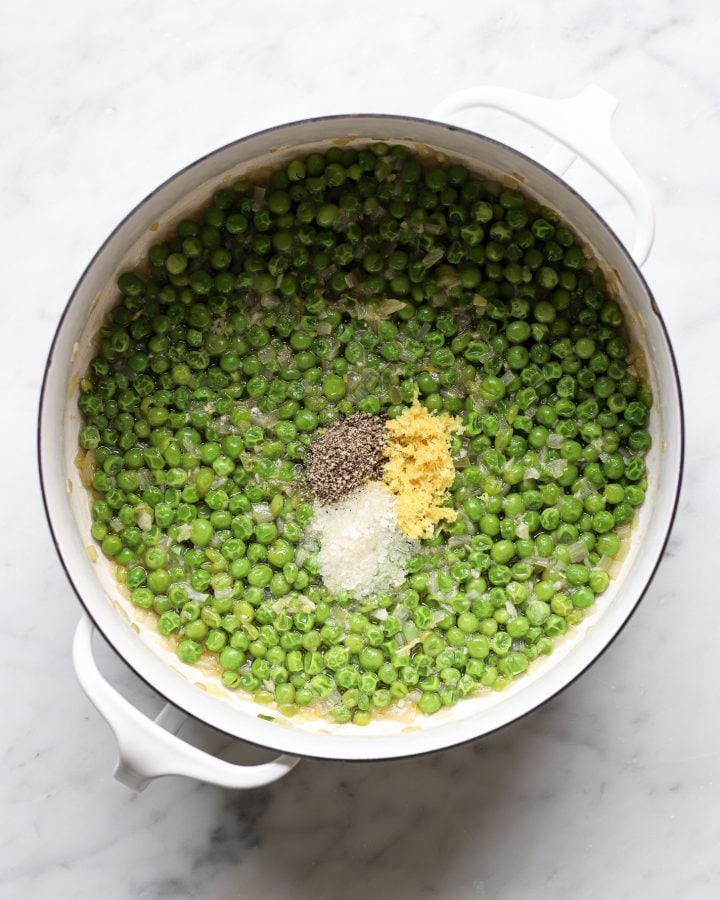 Cooked peas in a white Dutch oven with lemon zest, salt and pepper on top.