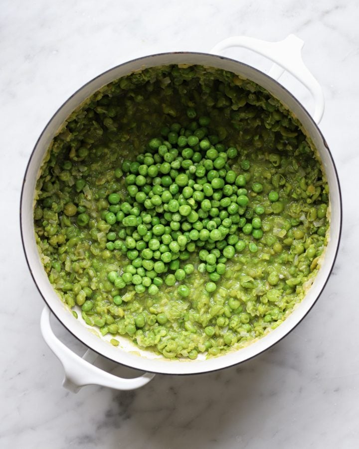 More peas on top of partially mashed peas in a white Dutch oven. 