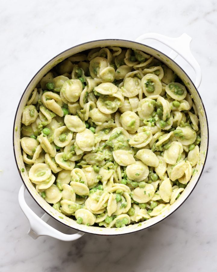 Cooked pasta stirred in to creamy pea sauce in a white pot.