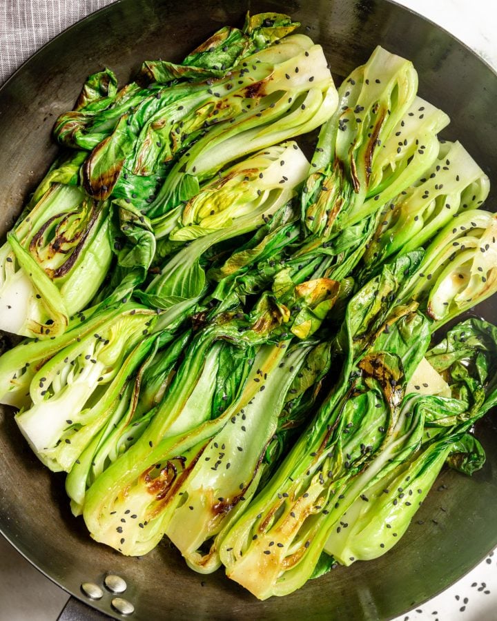 Seared bok choy in a skillet topped with sesame seeds.