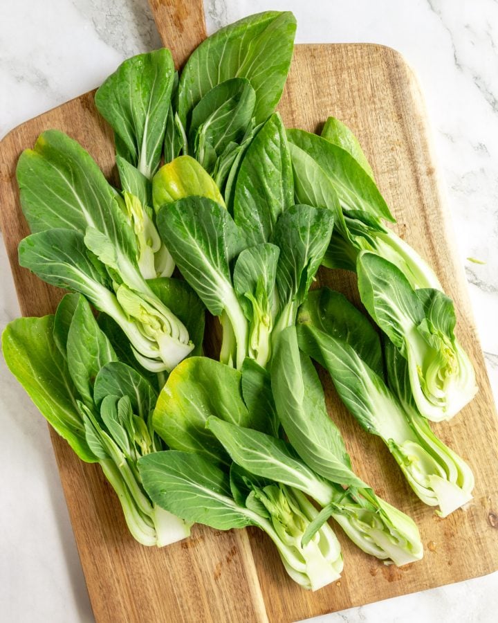 Halved baby bok choy on a wooden cutting board