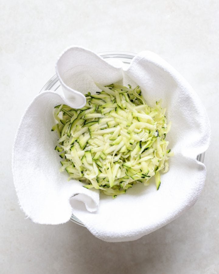 Grated zucchini in kitchen cloth in bowl.
