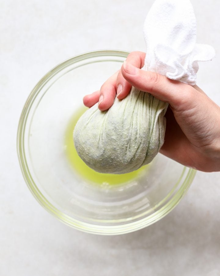 Hand squeezing out grated zucchini into a bowl 