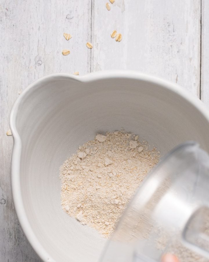 Oat flour mixture being poured out of blender and into a medium white mixing bowl 