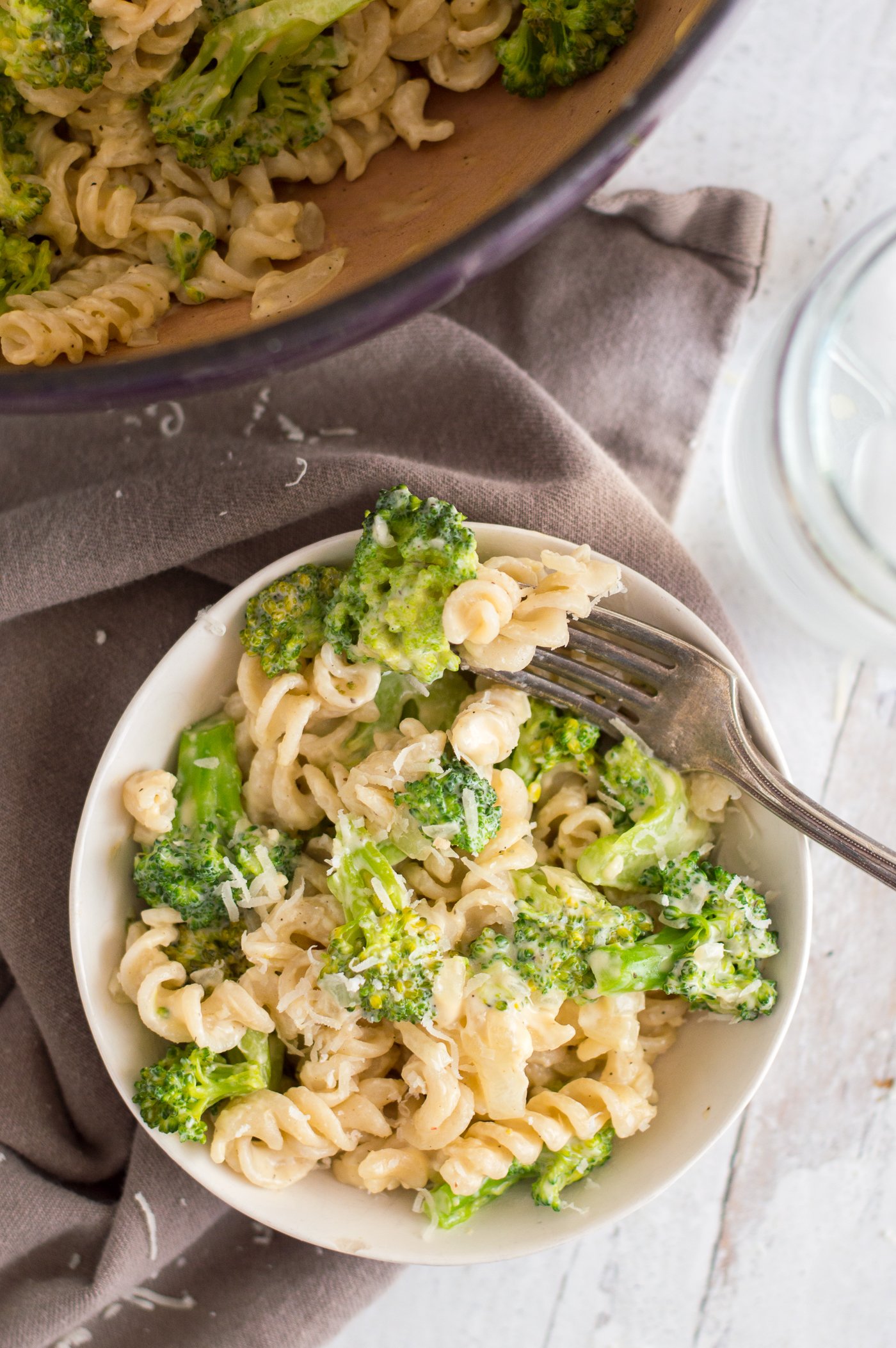 Creamy broccoli pasta in a bowl with a fork on a table with gray napkin.