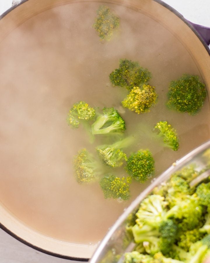 Broccoli florets being poured into a steaming pot of water.