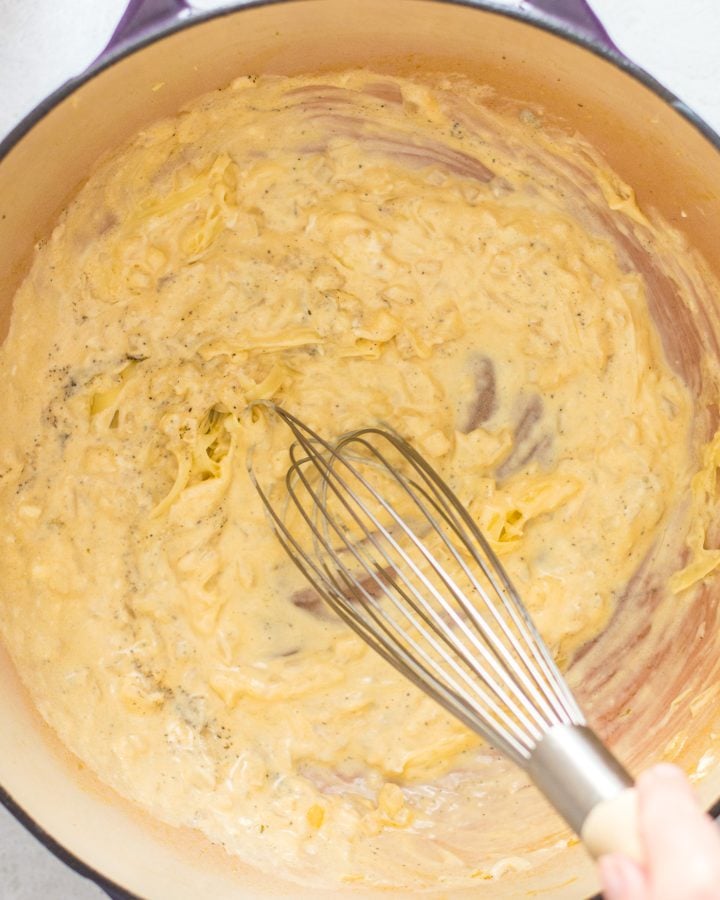 Cheese sauce for creamy broccoli pasta in a Dutch oven with a whisk.