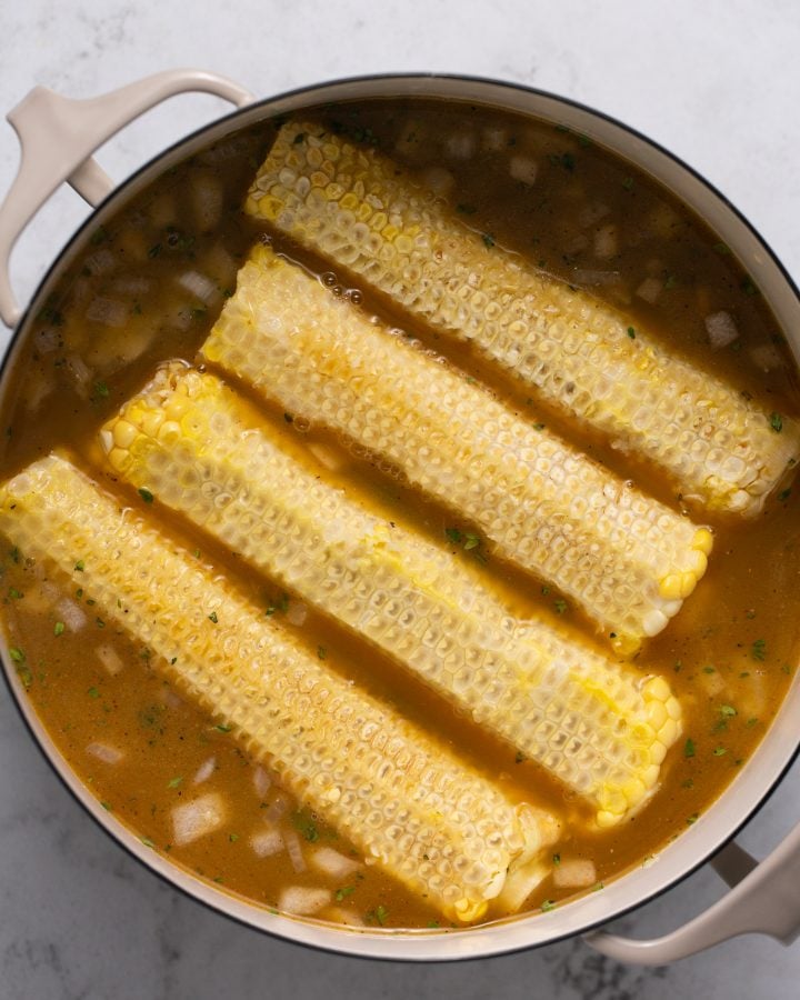 Corn cobs in a Dutch oven with vegetable broth and sauteed veggies.