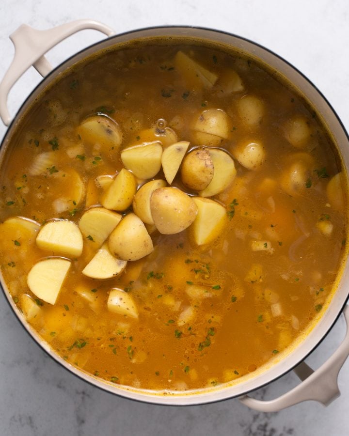 Yellow potatoes in a pot with vegetable broth and sauteed celery and onions. 