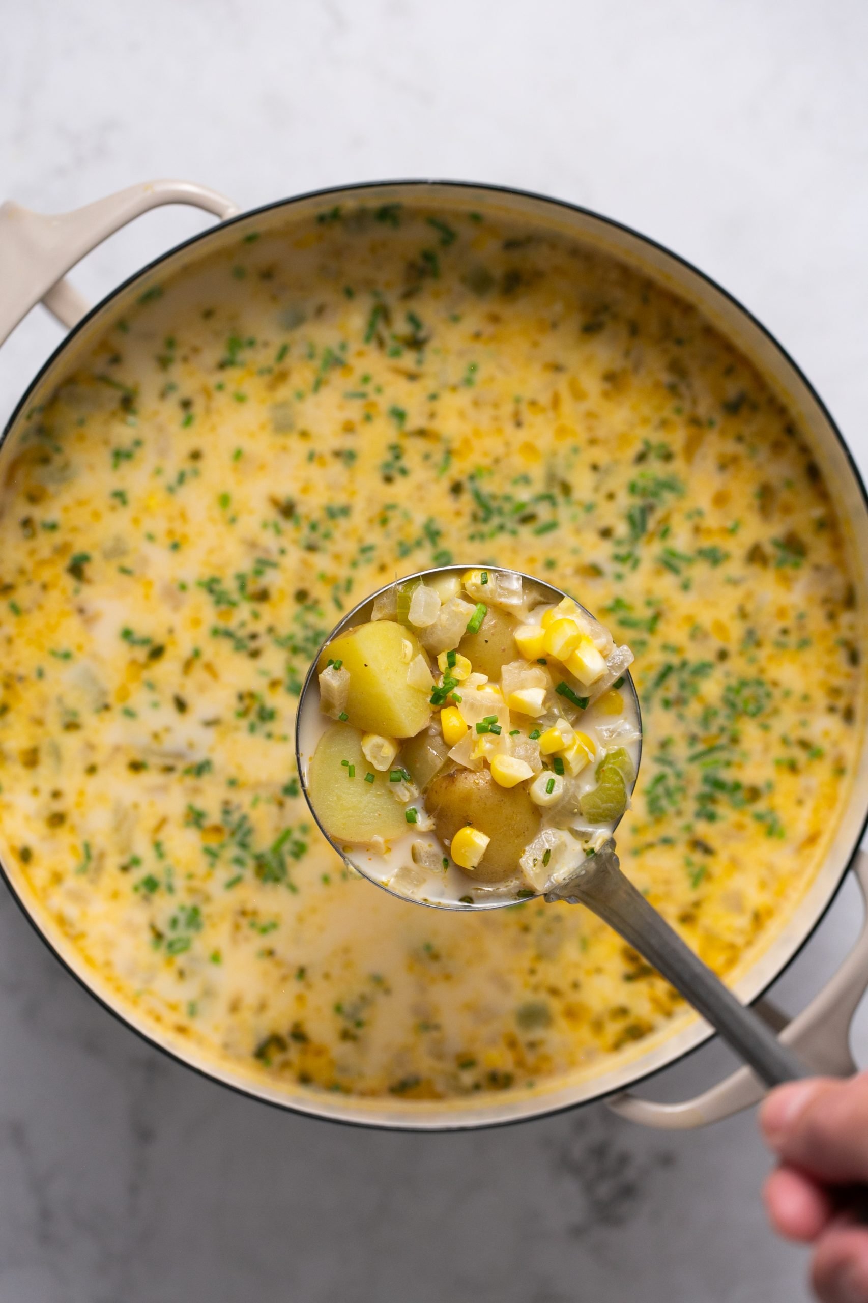 A ladle taking a scoop of corn and potato chowder out of the pot. 