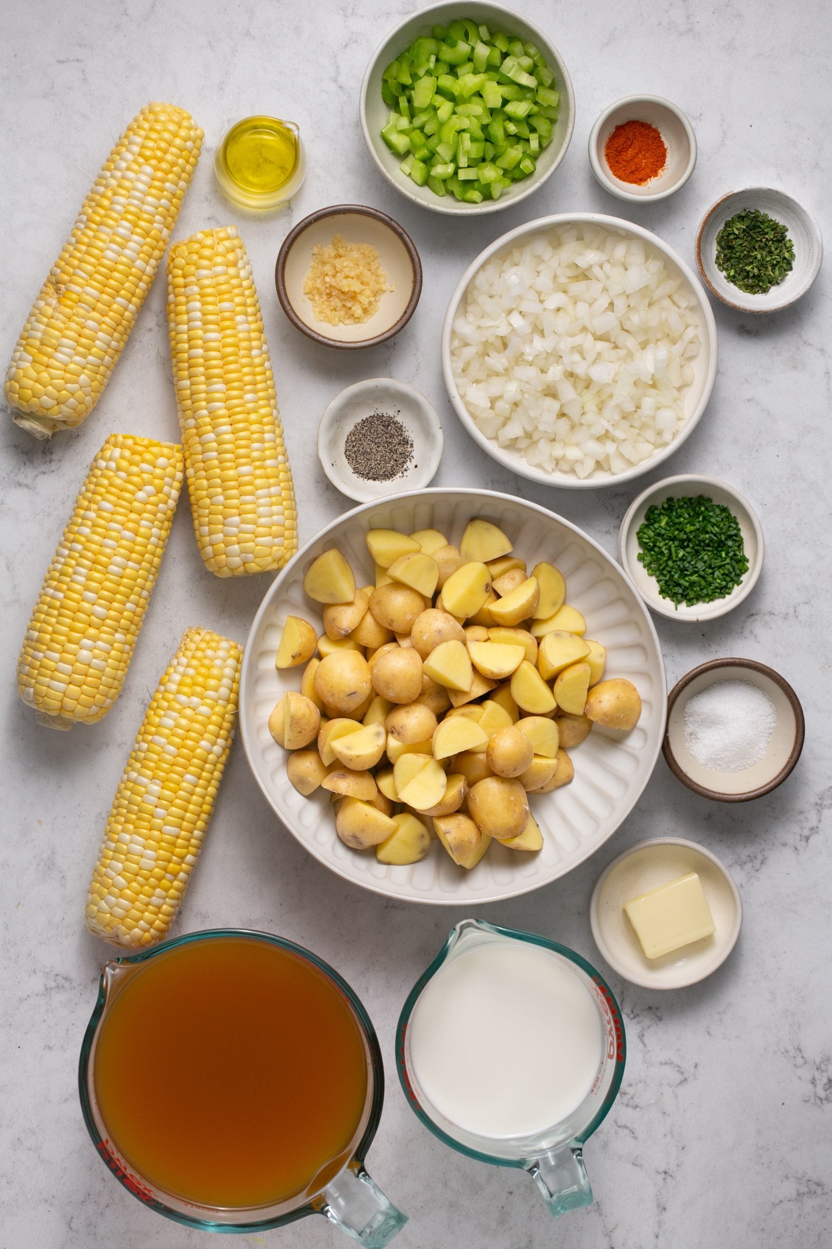 Ingredients for corn and potato chowder in a table in bowls and measuring cups.