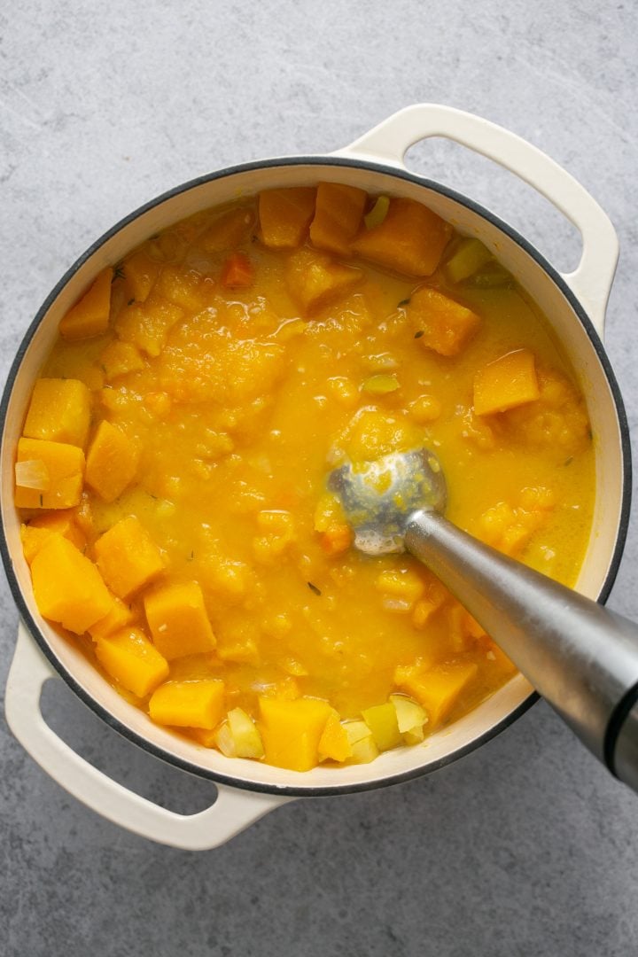 An immersion blender pureeing cooked ingredients for butternut squash soup.