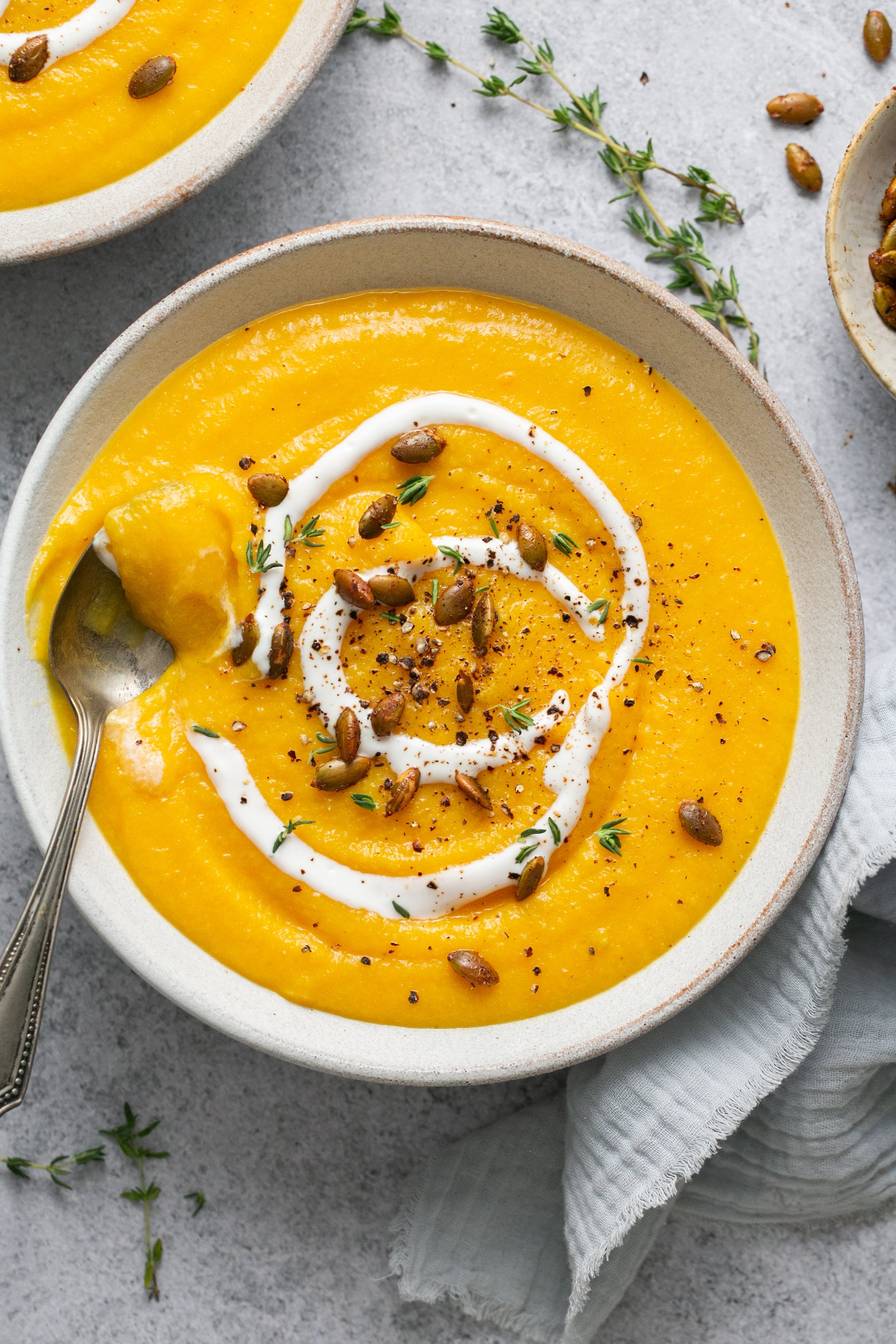 A bowl of butternut squash soup with a spoon, topped with yogurt, thyme, and pepitas. 