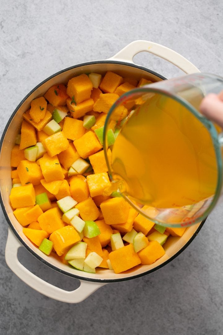 Broth being poured over butternut squash and diced apples in a pot