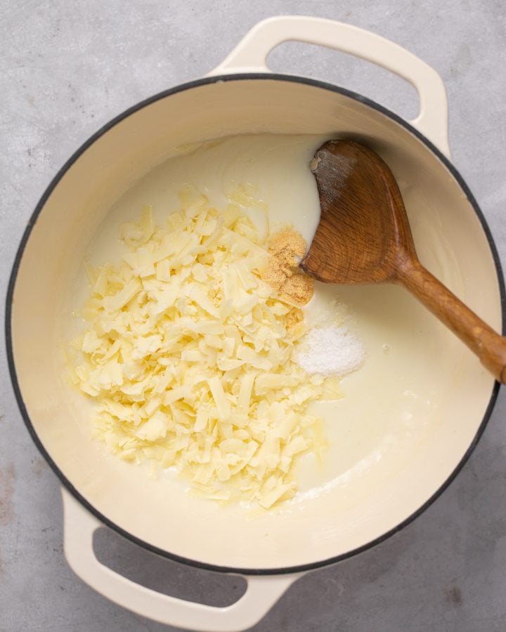 Grated white cheddar , salt and garlic powder in a pot with milk roux mixture with a wooden spoon.
