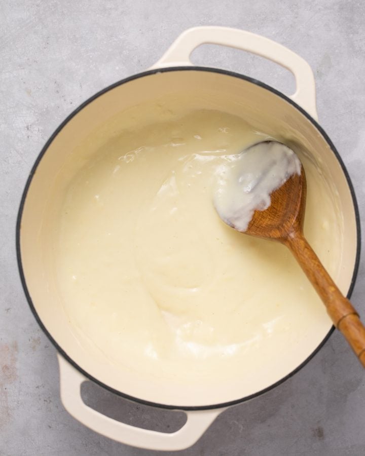Cheese sauce stirred together in a a pot with a wooden spoon. 