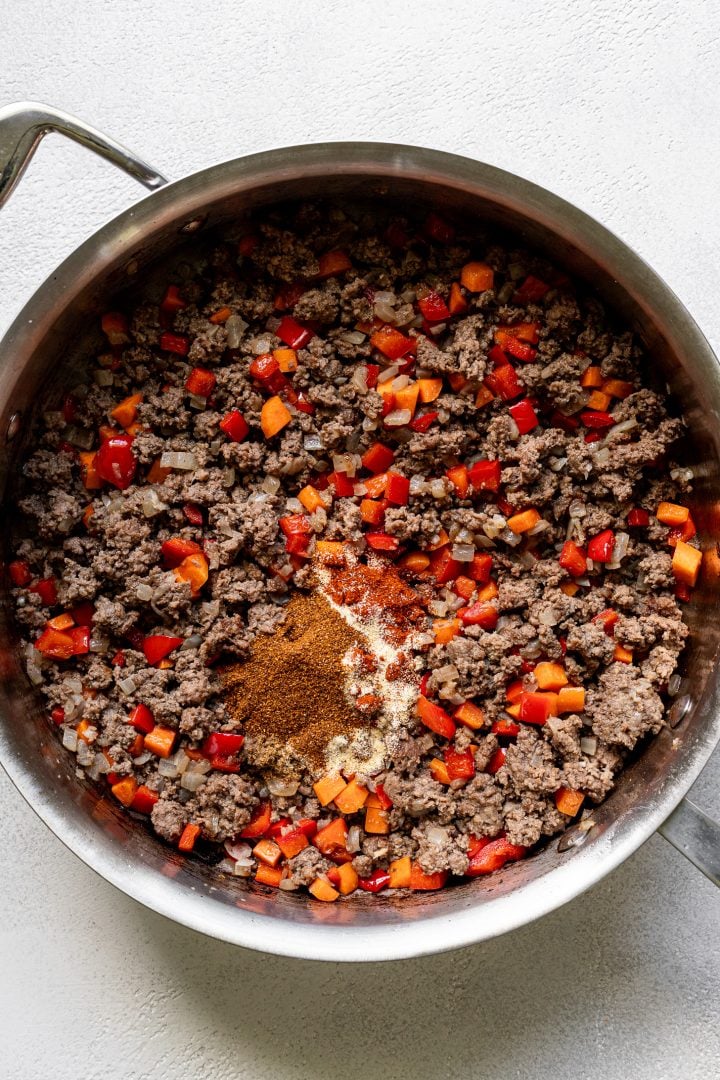 Cooked ground beef with veggies in a pot with spices on top before being stirred in.