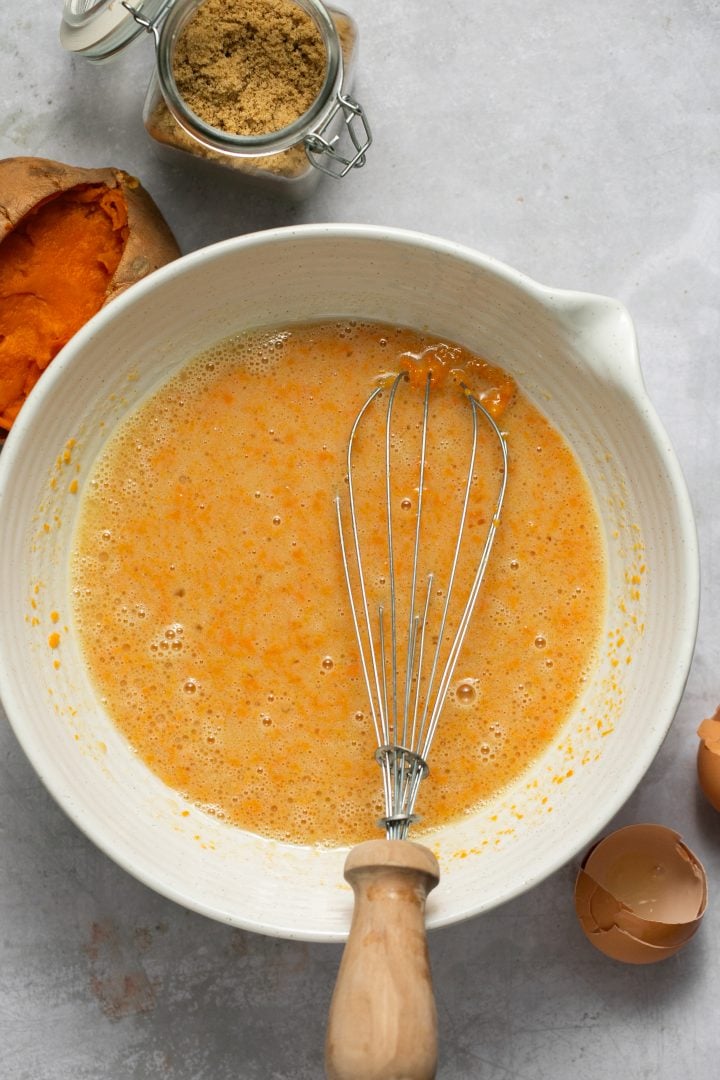 Wet ingredients for sweet potato cornbread mixed together in a bowl with a whisk.
