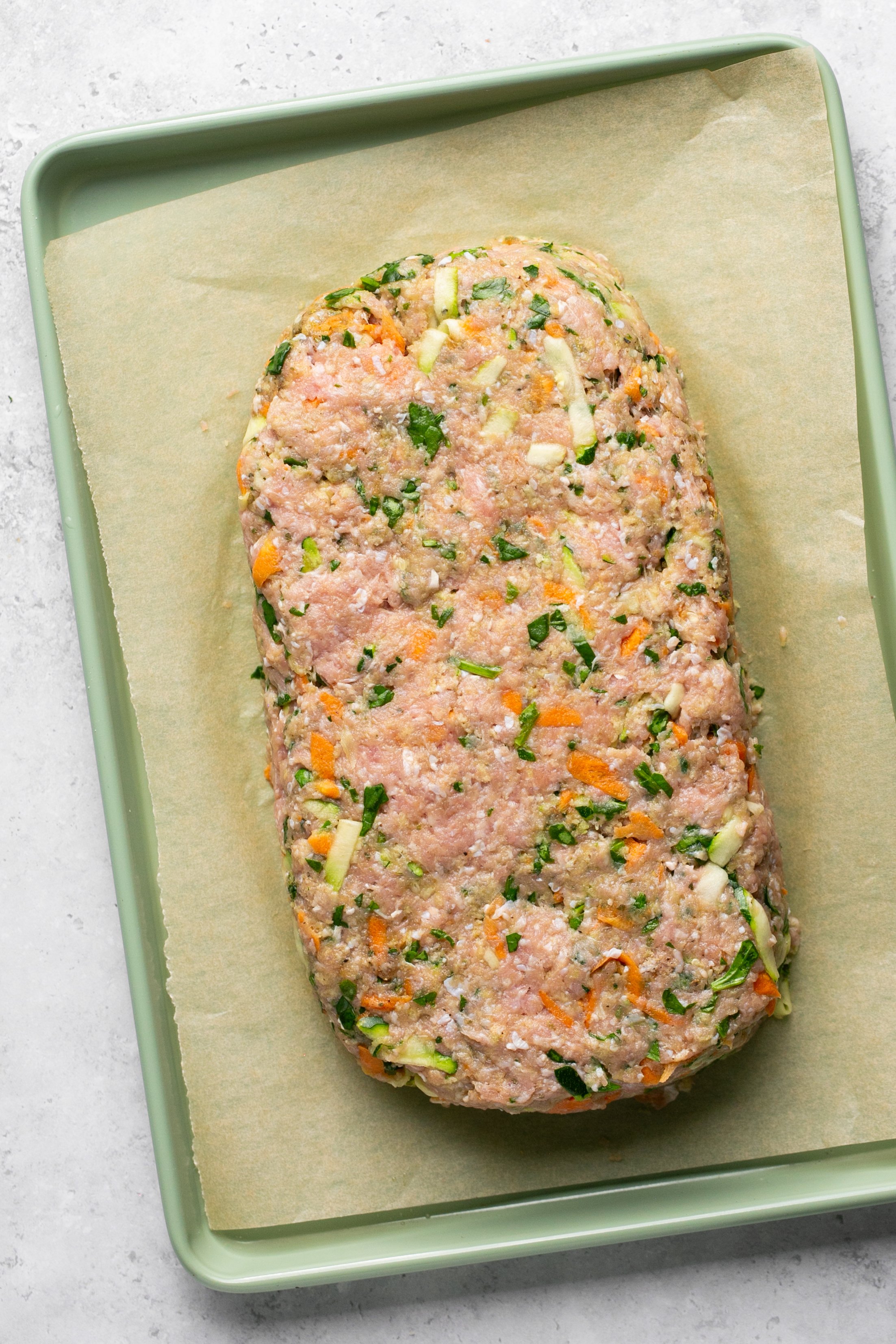 Raw turkey meatloaf mixture shaped into a rectangular loaf sitting on a parchment lined baking sheet on a white counter.