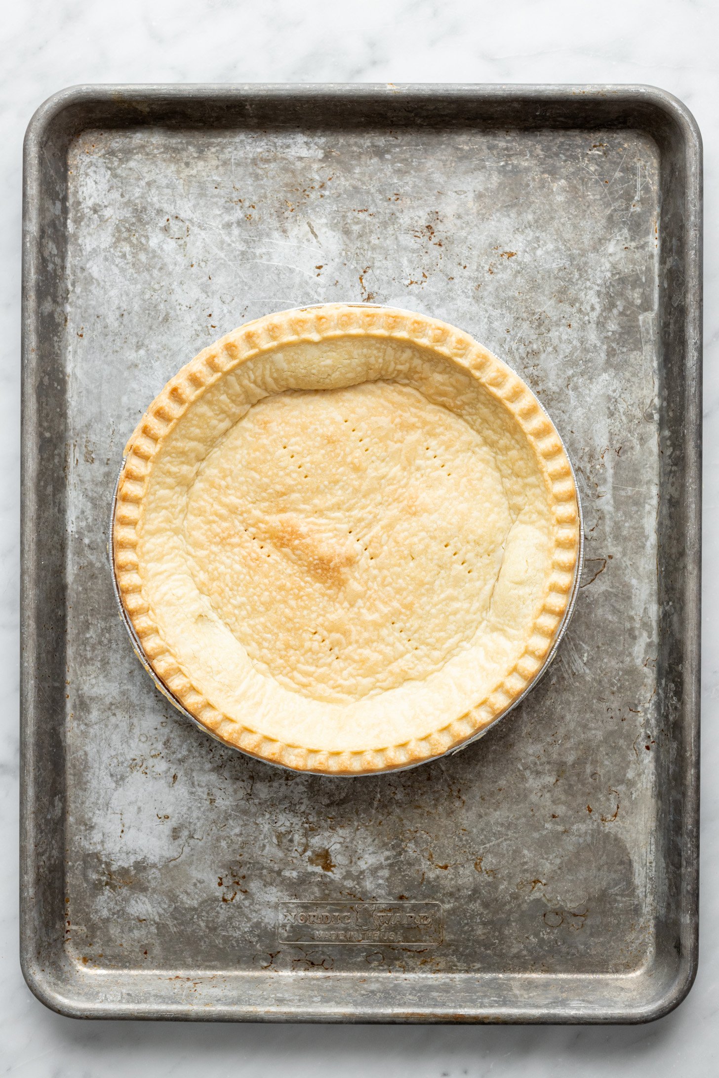 Cooked pie crust in a pie tin sitting on a baking sheet.