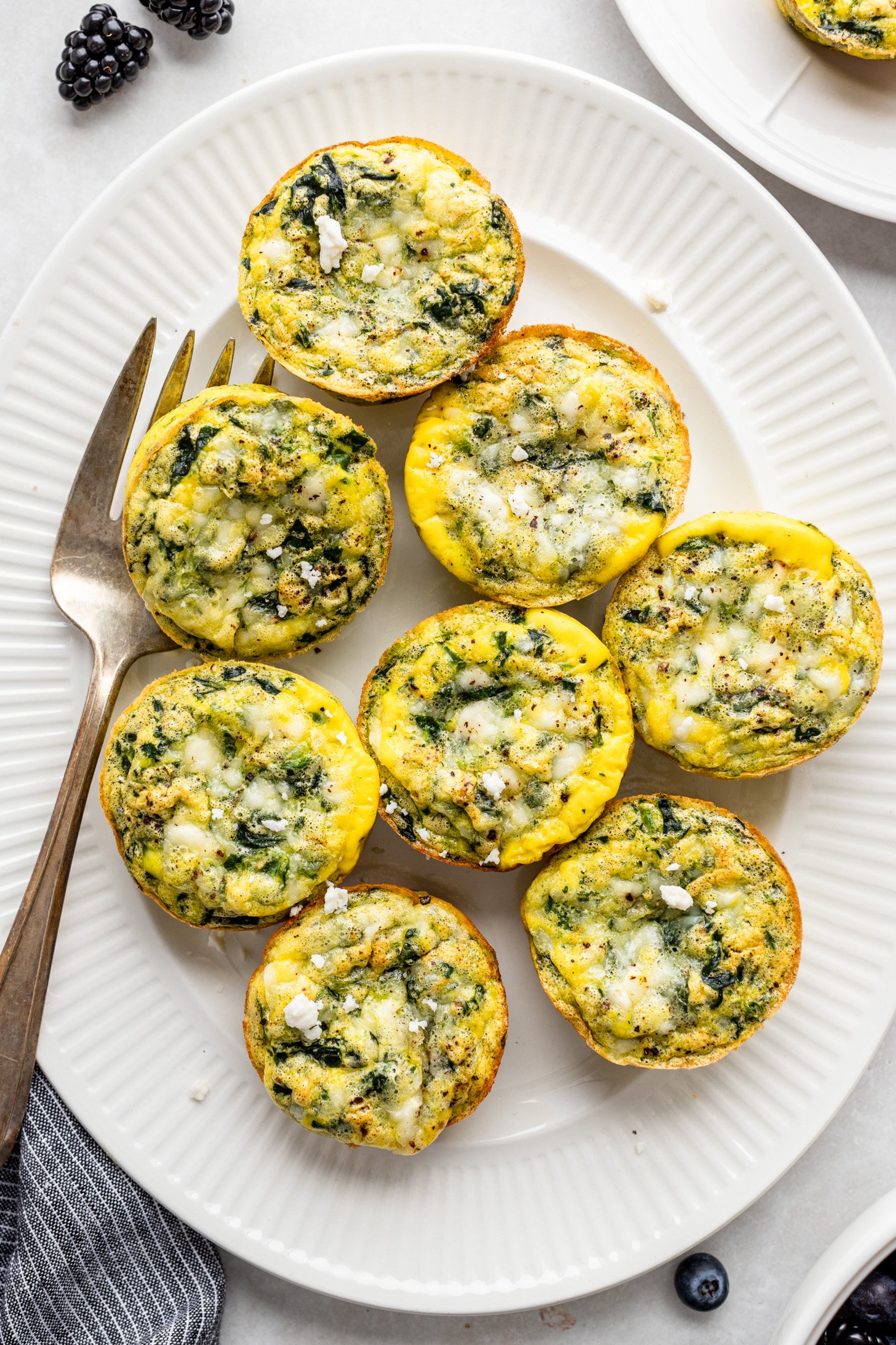 Spinach feta eggs cups on a white platter with a large serving fork.