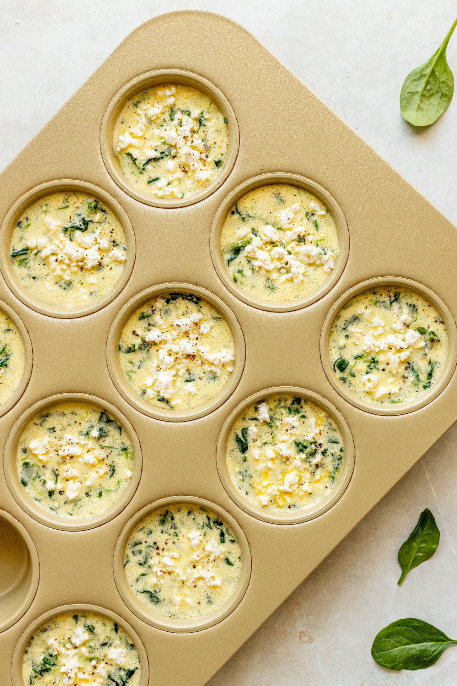 Spinach feta eggs cups in a muffin tin before baking. 